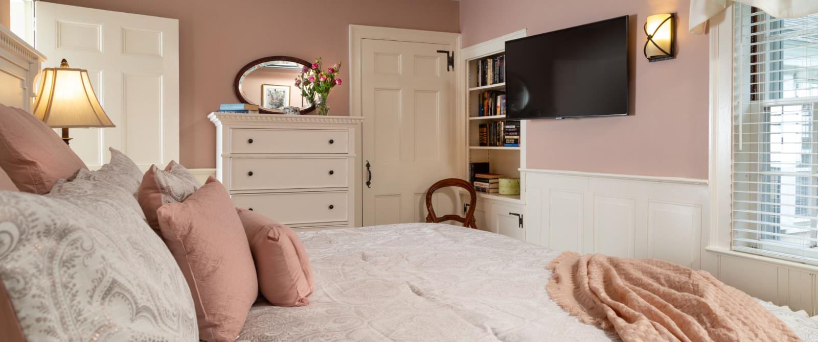 Bedroom with peach walls, white trim, light paisley bedding, white dresser, and wall-mounted flat-screen TV