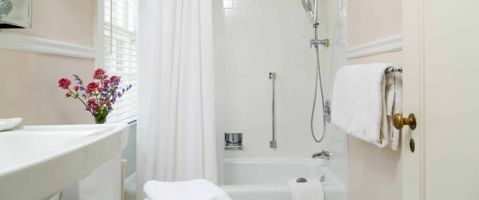 Bathroom with light colored walls, white trim, white sink, and white tub with shower