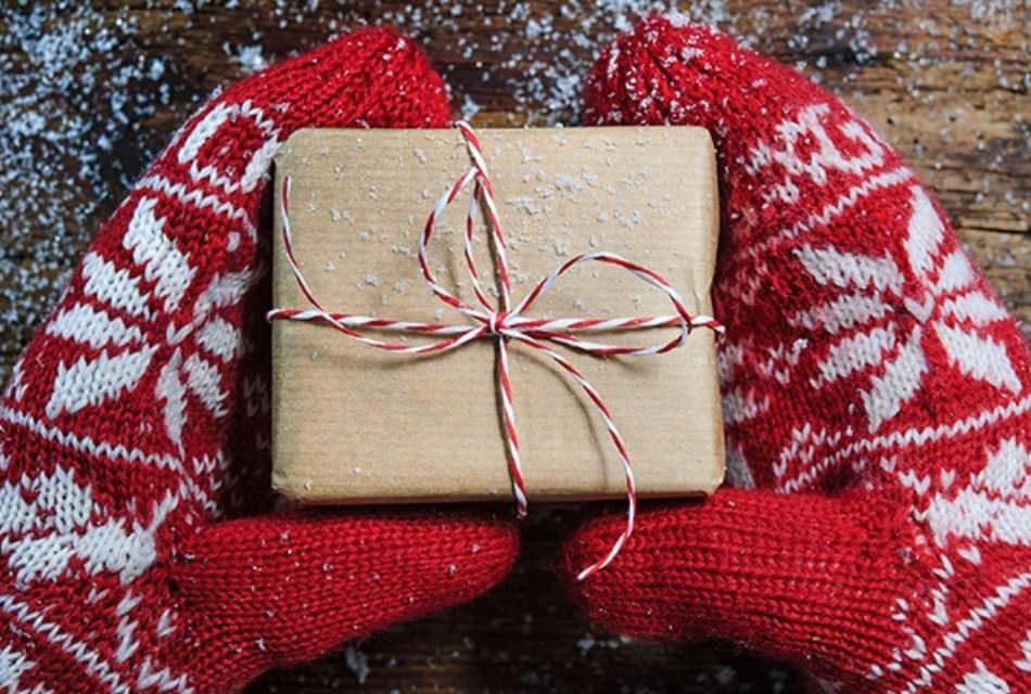 Person with red and white mittens holding a small packge wrapped in kraft paper and red and white twine