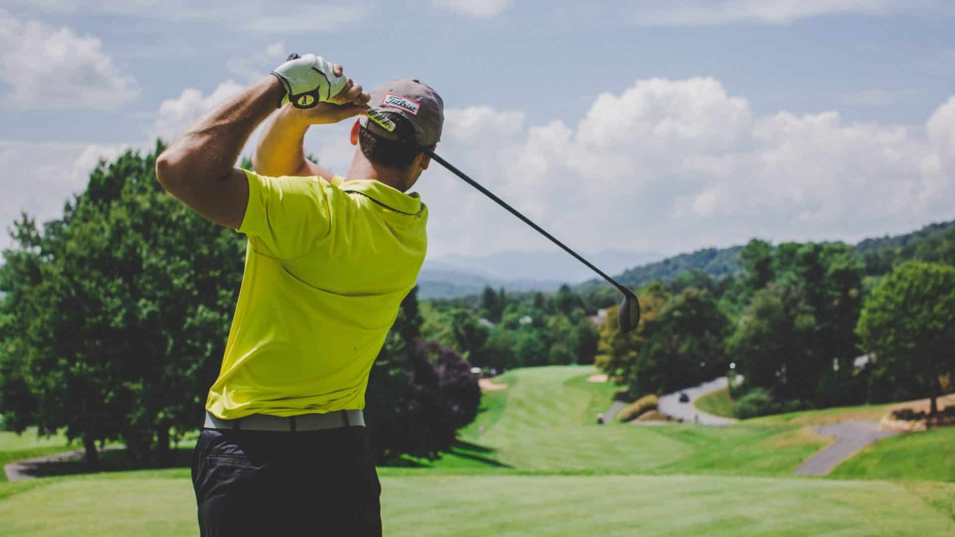 Man swinging a golf club on a green golf course