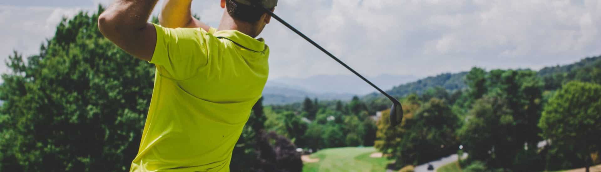 Man swinging a golf club on a green golf course