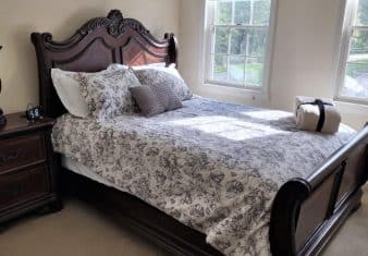 Bedroom with light colored walls and carpetting, dark wooden sleigh bed, floral bedding, wooden dresser, and windows