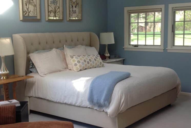 Bedroom with blue walls, white trim, upholstered headboard, white bedding, and multiple windows