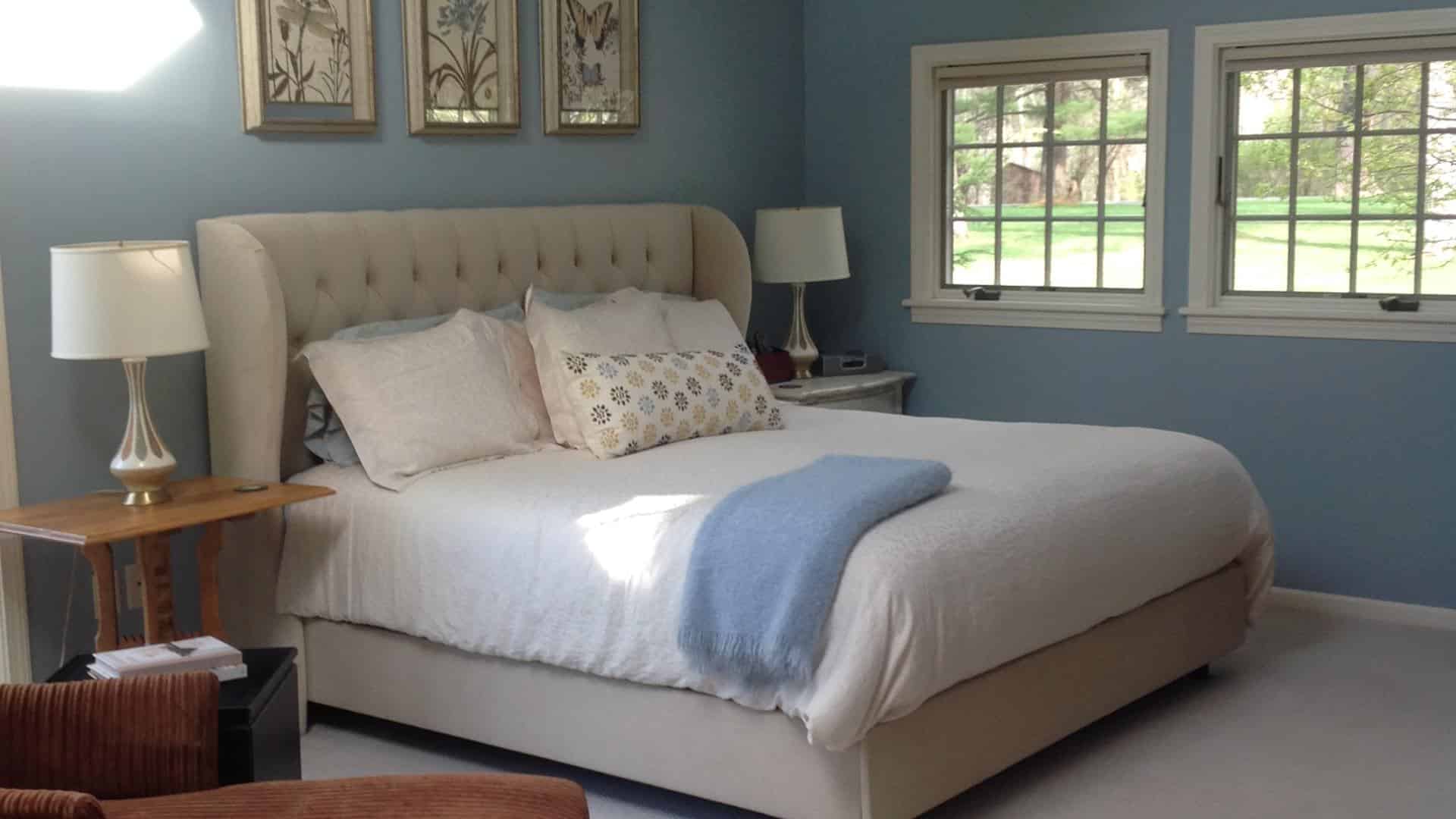 Bedroom with blue walls, white trim, upholstered headboard, white bedding, and multiple windows