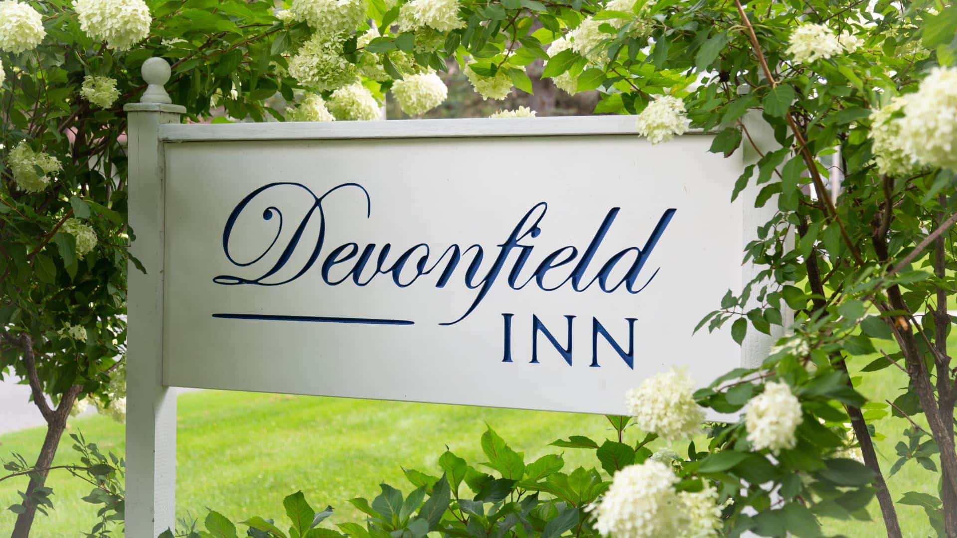 Close up view of a sign showing Devonfield Inn surrounded by white flowers