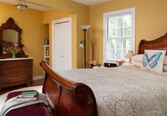 Bedroom with yellow walls, white trim, hardwood flooring, wooden sleigh bed, wooden dresser, and window