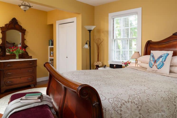 Bedroom with yellow walls, white trim, hardwood flooring, wooden sleigh bed, wooden dresser, and window