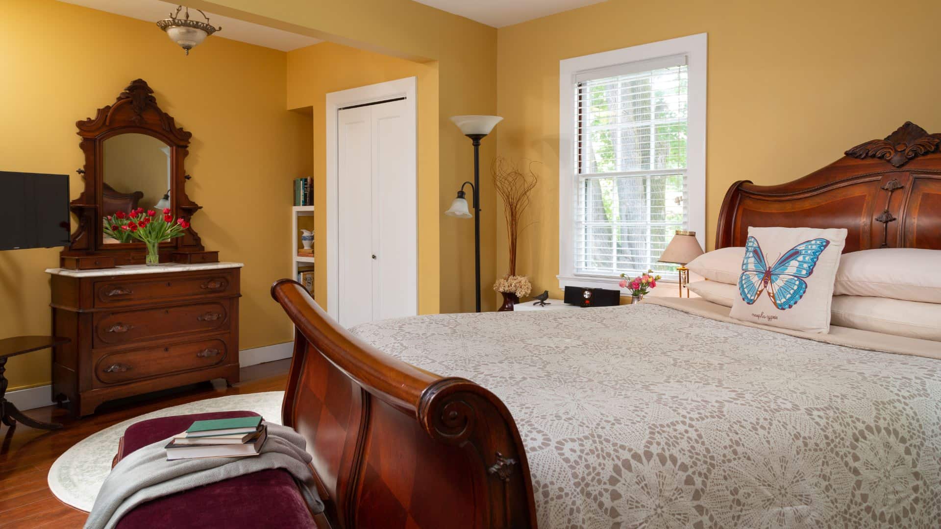 Bedroom with yellow walls, white trim, hardwood flooring, wooden sleigh bed, wooden dresser, and window