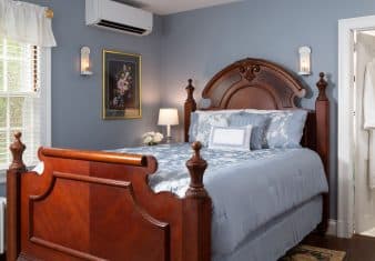 Bedroom with blue walls, hardwood flooring, wooden bed, blue bedding, and view into bathroom