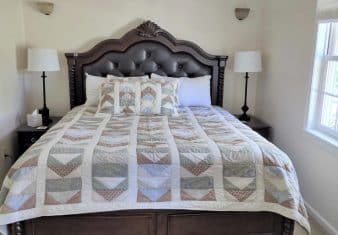 Bedroom with white walls, dark wood and leather upholstered headboard, multicolored bedding, two nightstands, and two lamps