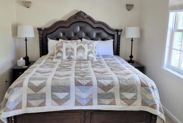 Bedroom with white walls, dark wood and leather upholstered headboard, multicolored bedding, two nightstands, and two lamps