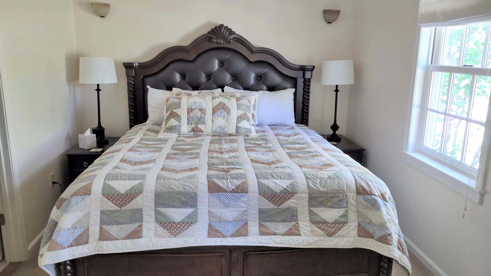 Bedroom with white walls, dark wood and leather upholstered headboard, multicolored bedding, two nightstands, and two lamps