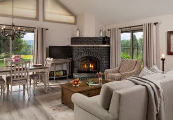 Large gathering area with light colored walls, hardwood flooring, upholstered sofa and chair, wooden coffee table, fireplace, and dining area