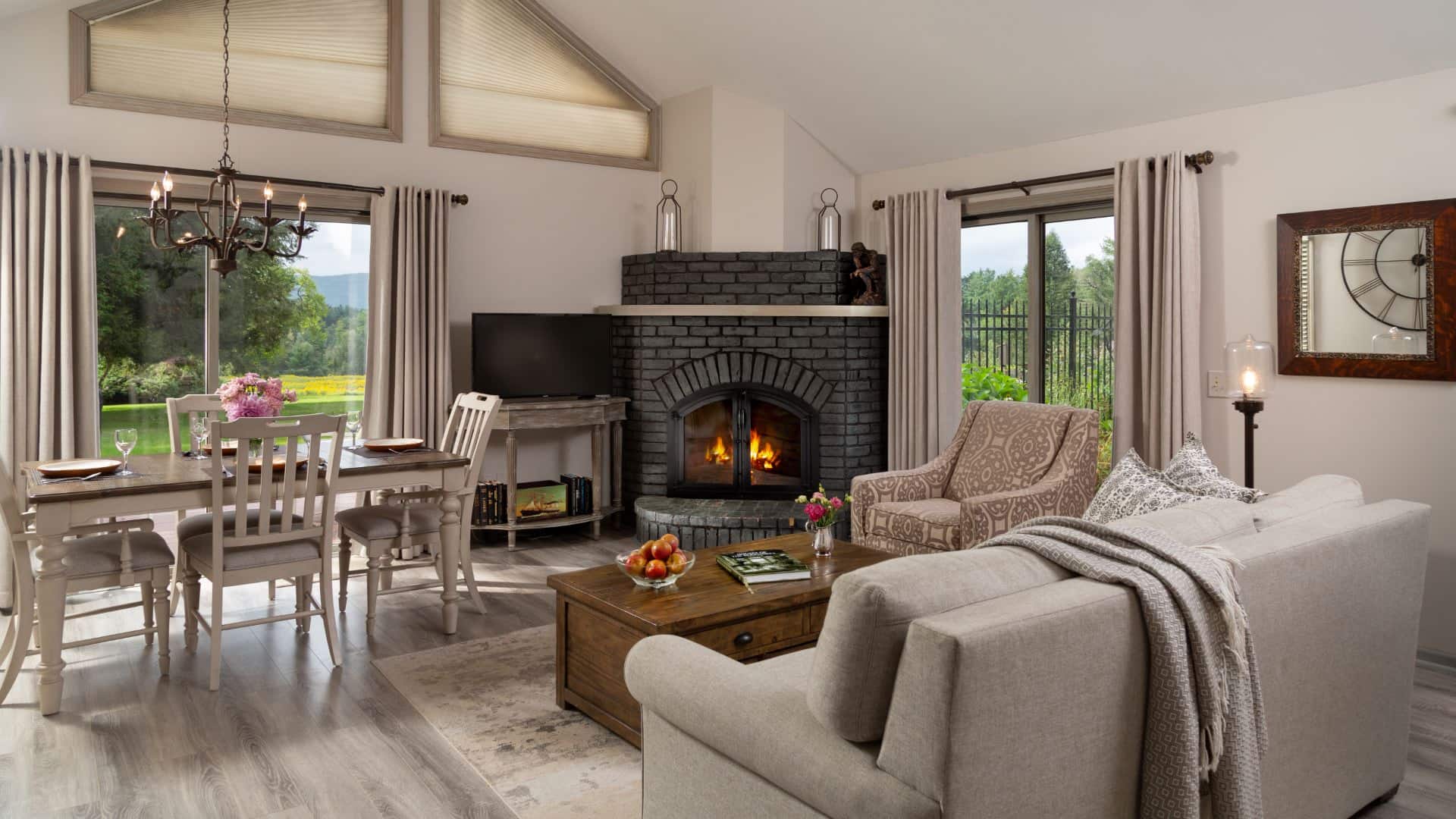 Large gathering area with light colored walls, hardwood flooring, upholstered sofa and chair, wooden coffee table, fireplace, and dining area