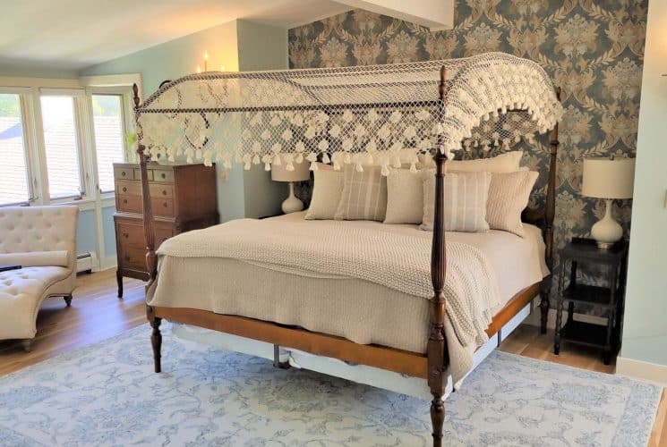 Bedroom with light blue walls, white trim, hardwood flooring, wooden four-poster bed, tan bedding, chaise, and wooden dresser