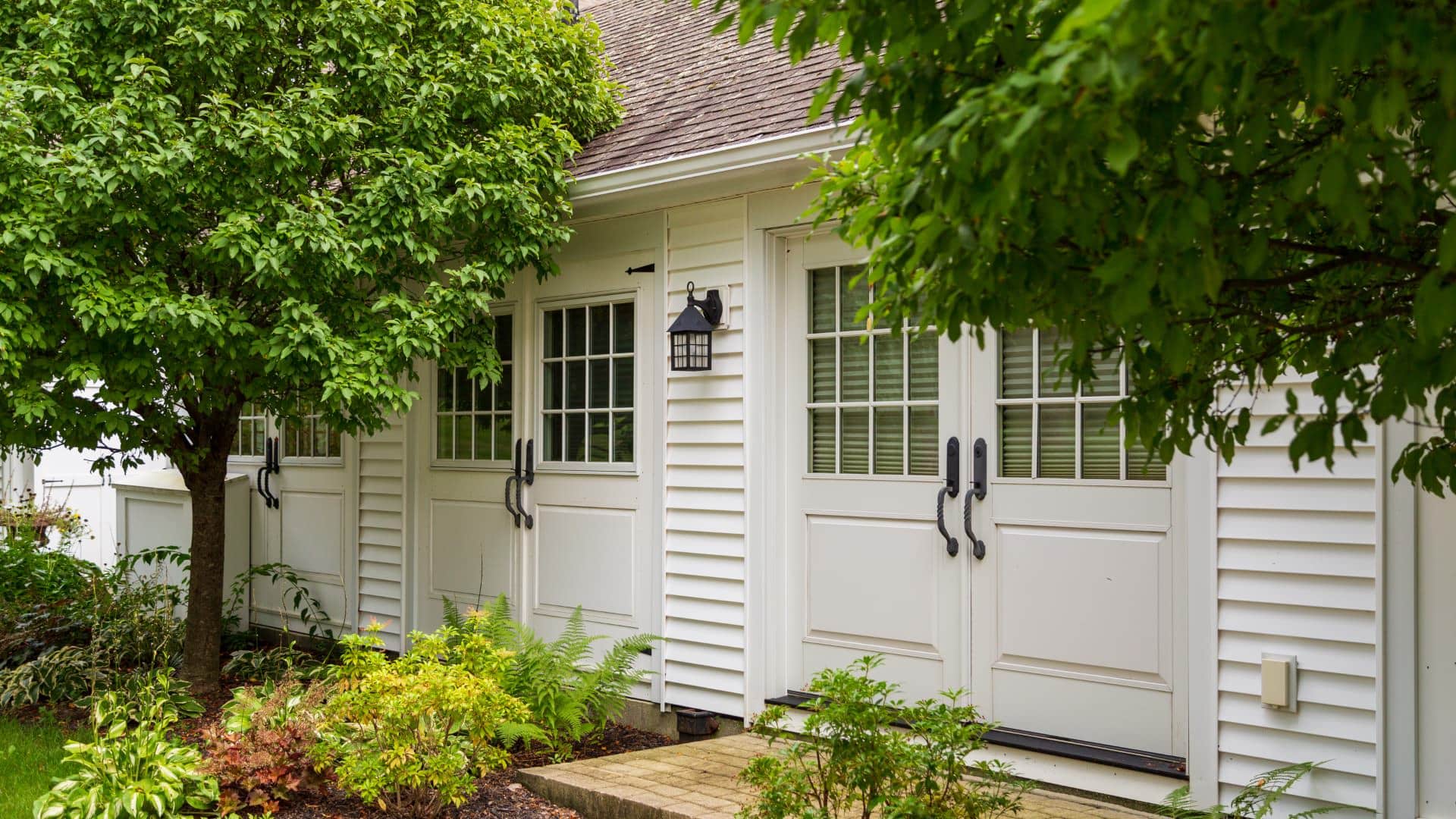 Close up exterior view of the property painted white and surrounded by large green trees and shrubs