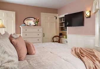 Bedroom with peach walls, white trim, light paisley bedding, white dresser, and wall-mounted flat-screen TV