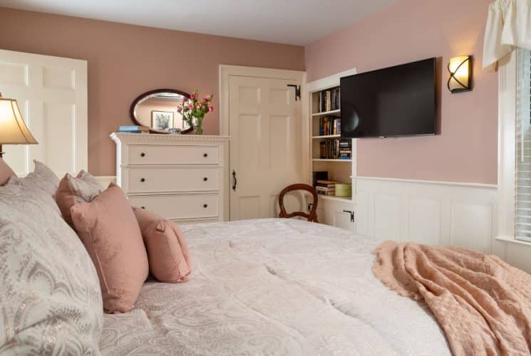 Bedroom with peach walls, white trim, light paisley bedding, white dresser, and wall-mounted flat-screen TV