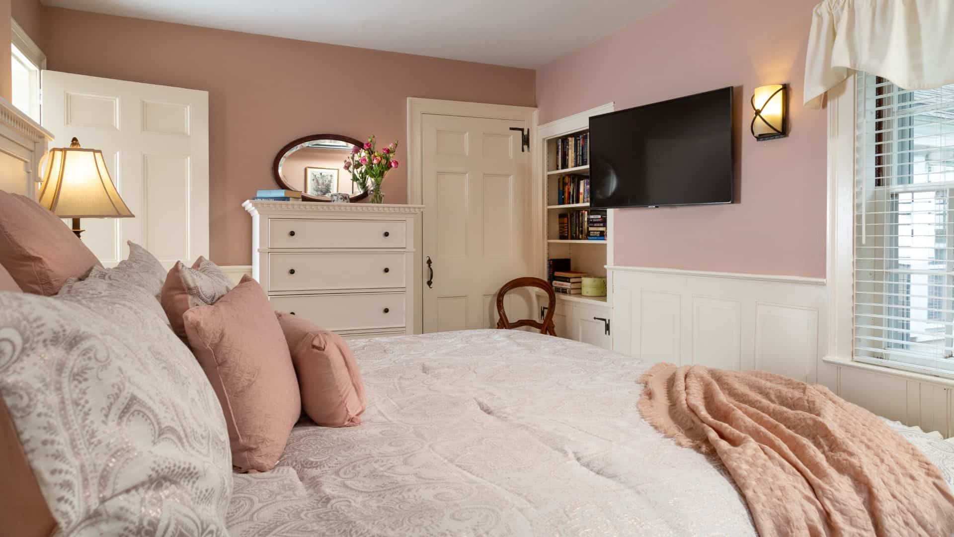 Bedroom with peach walls, white trim, light paisley bedding, white dresser, and wall-mounted flat-screen TV