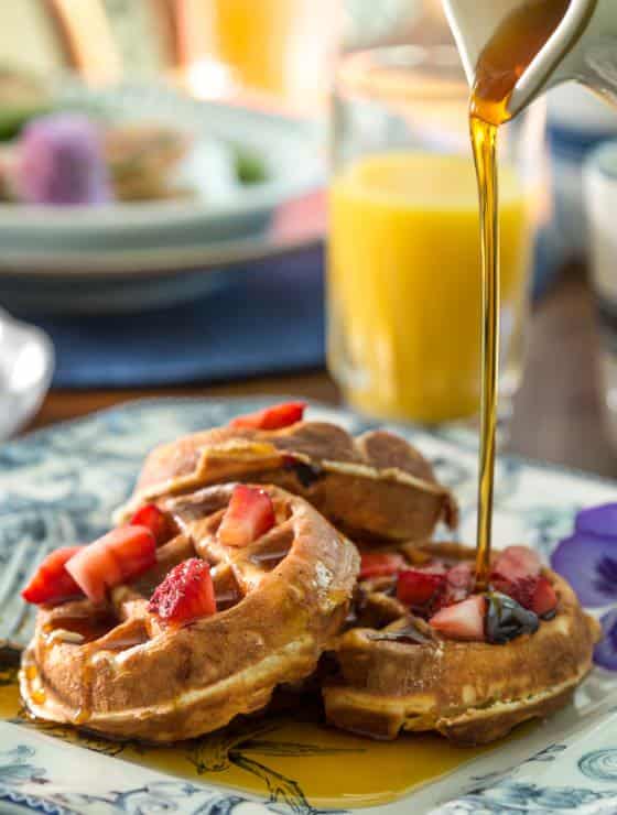 Square blue and white plate full of belgian waffles covered in strawberries and syrup