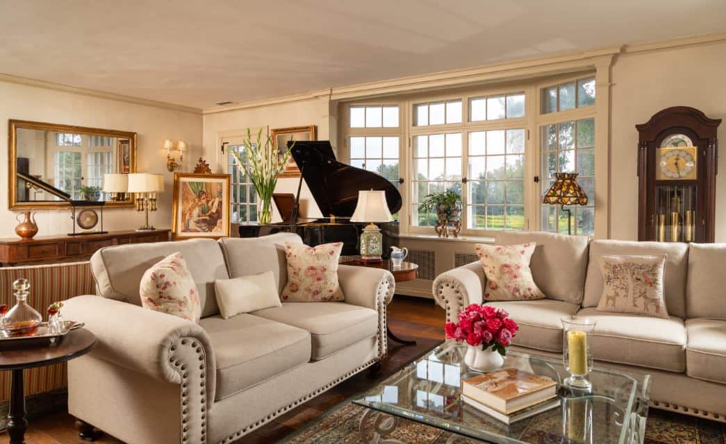 Large gathering room with cream walls, hardwood flooring, upholstered sofas, glass coffee table, grand piano, and grandfather clock at the Devonfield Inn