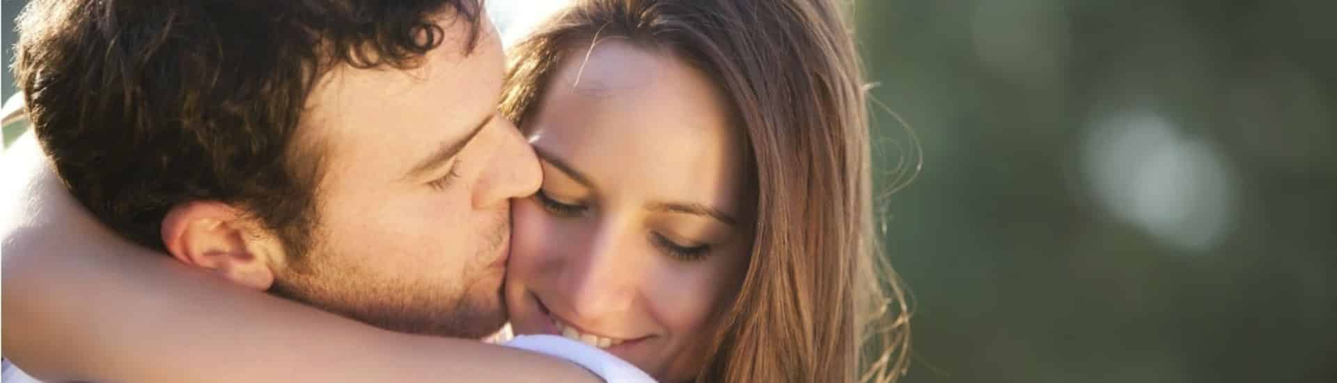 Close up view of woman hugging man who is kissing the woman on the cheek