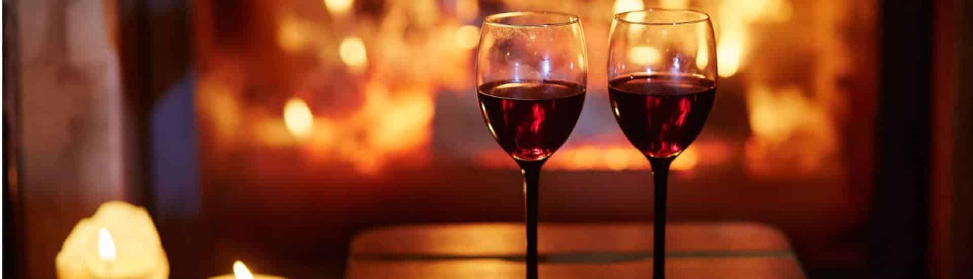 Two wine glasses filled with red wine with fireplace blurred in the background