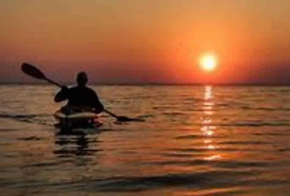 Person kayaking with the sun setting in the background