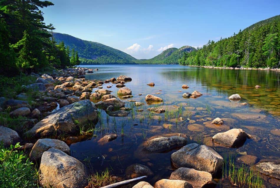 Small lake with still water surrounded by rocks and green trees