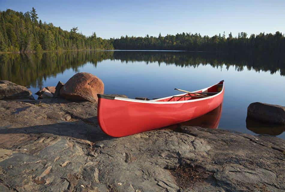 Red canoe resting on large rock near lake with still water surrounded by green trees