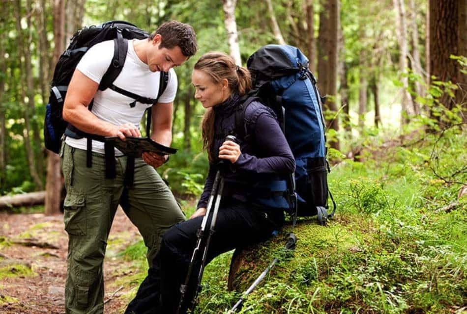 Man and woman looking at a map while hiking on a path surrounded by trees