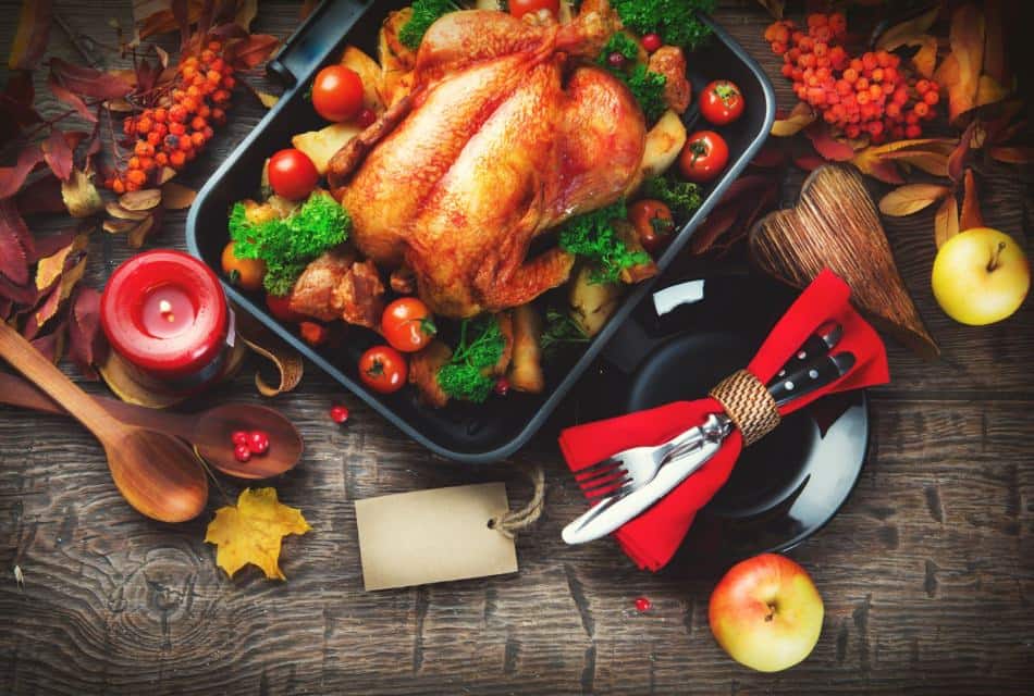 Close up view of a roasted turkey in a pan surrounded by potatoes, tomatoes, and parsley on a wooden table