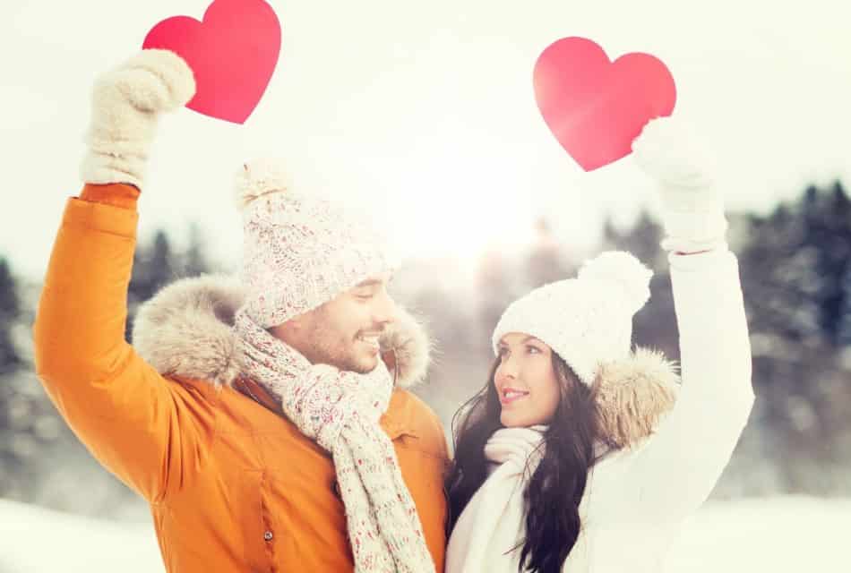 Man and woman dressed in winter gear holding red hearts