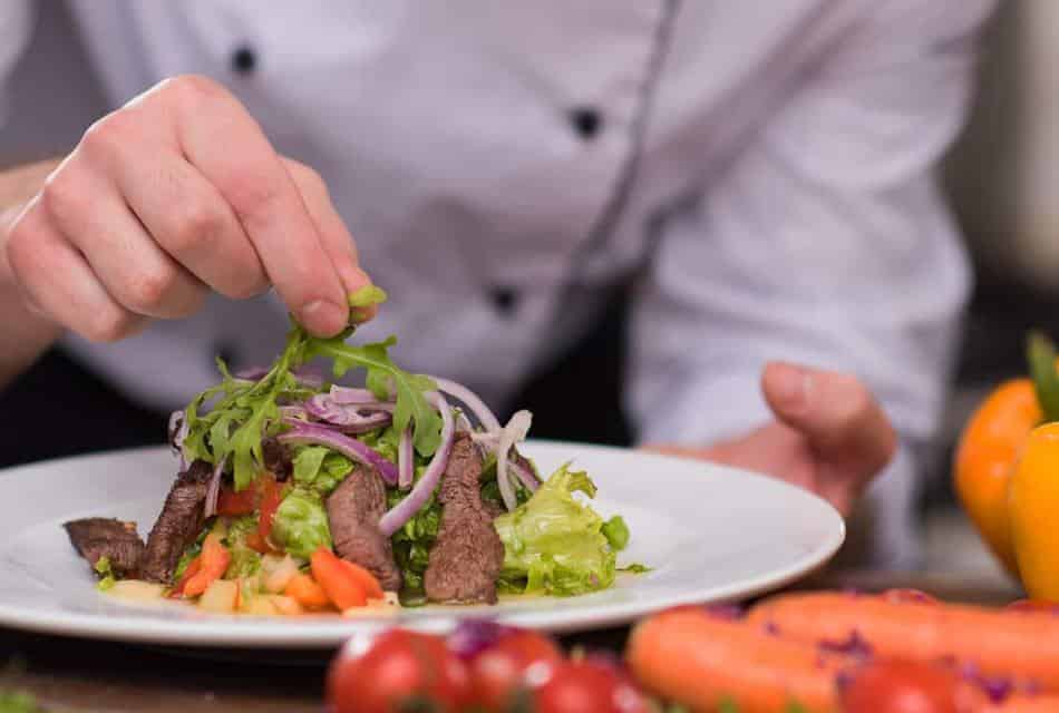 Close up view of a salad topped with steak on a white plate