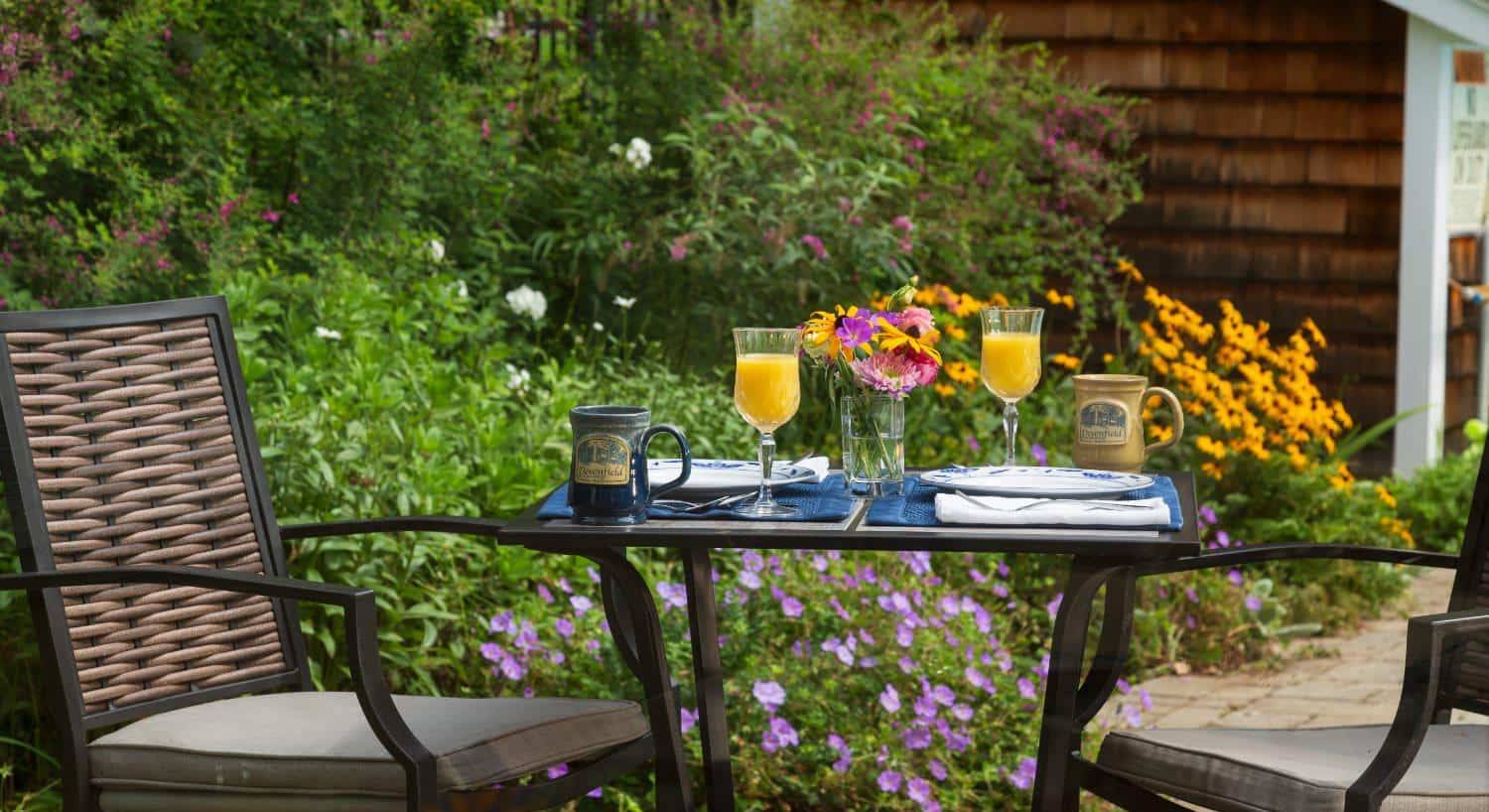 Small patio table with two chairs and colorful flowers and green vegetation in the background