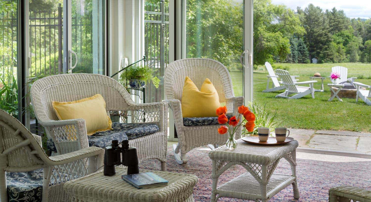 Sun room with white wicker patio furniture, opened sliding glass doors, and view of the firepit area with white adirondack chairs