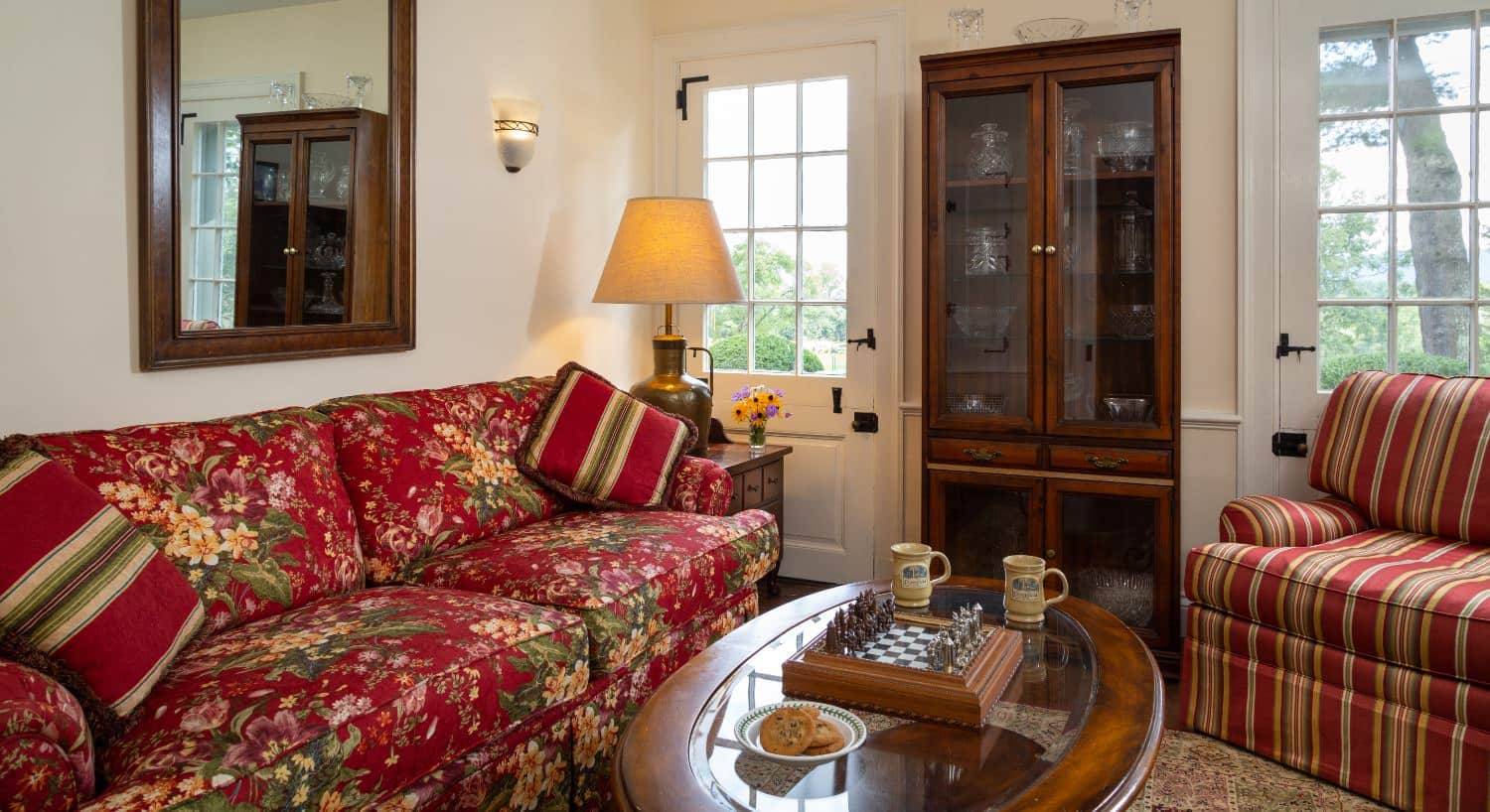 Sitting area with upholstered floral sofa and striped upholstered chair, wooden with glass inlay coffee table, and wooden bookcase