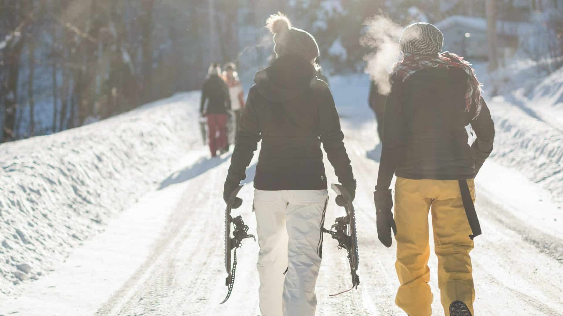 People carrying their snowshoes down a snowy trail between trees